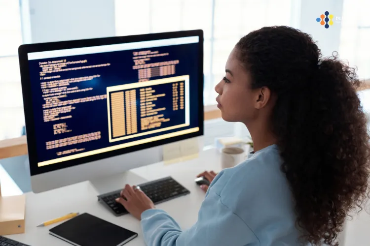A woman sits at a desk looking at a computer.
