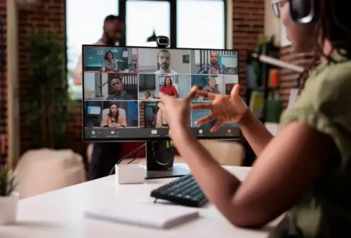 A woman sits at her desk in a team meeting with her nearshore dedicated team remotely tuning in on the monitor at her desk.