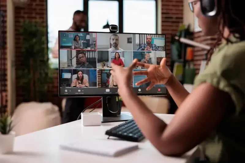 A woman sits at her desk in a team meeting with her nearshore dedicated team remotely tuning in on the monitor at her desk.