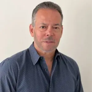 Ruben Santana, one of the LATAM talent acquisition specialists from Plugg Technologies stands in a blue shirt before a white wall, smiling for a corporate portrait.