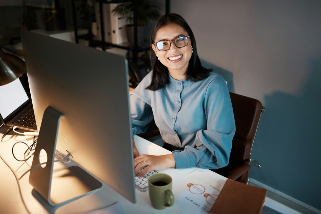 Pretty Latin American data engineer with glasses, smiling in front of laptop