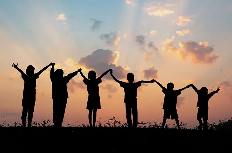 Children silouhetted by the sunset, raising hands together in celebration.