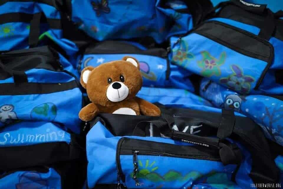 Blue duffle bags for called Sweet Cases with a brown teddy bear sitting on top