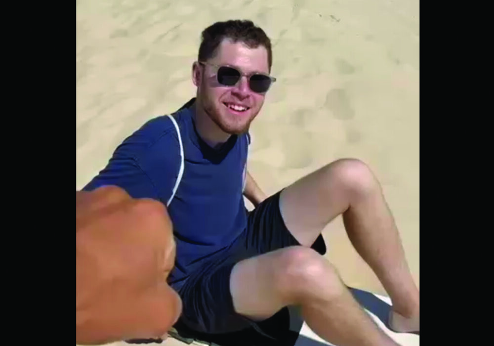 Evan Meyers sand dune surfing in Brazil while wearing a blue shirt and black shorts