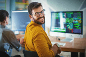 A nearshore salesforce director in a yellow shirt smiles in front of his computer desk